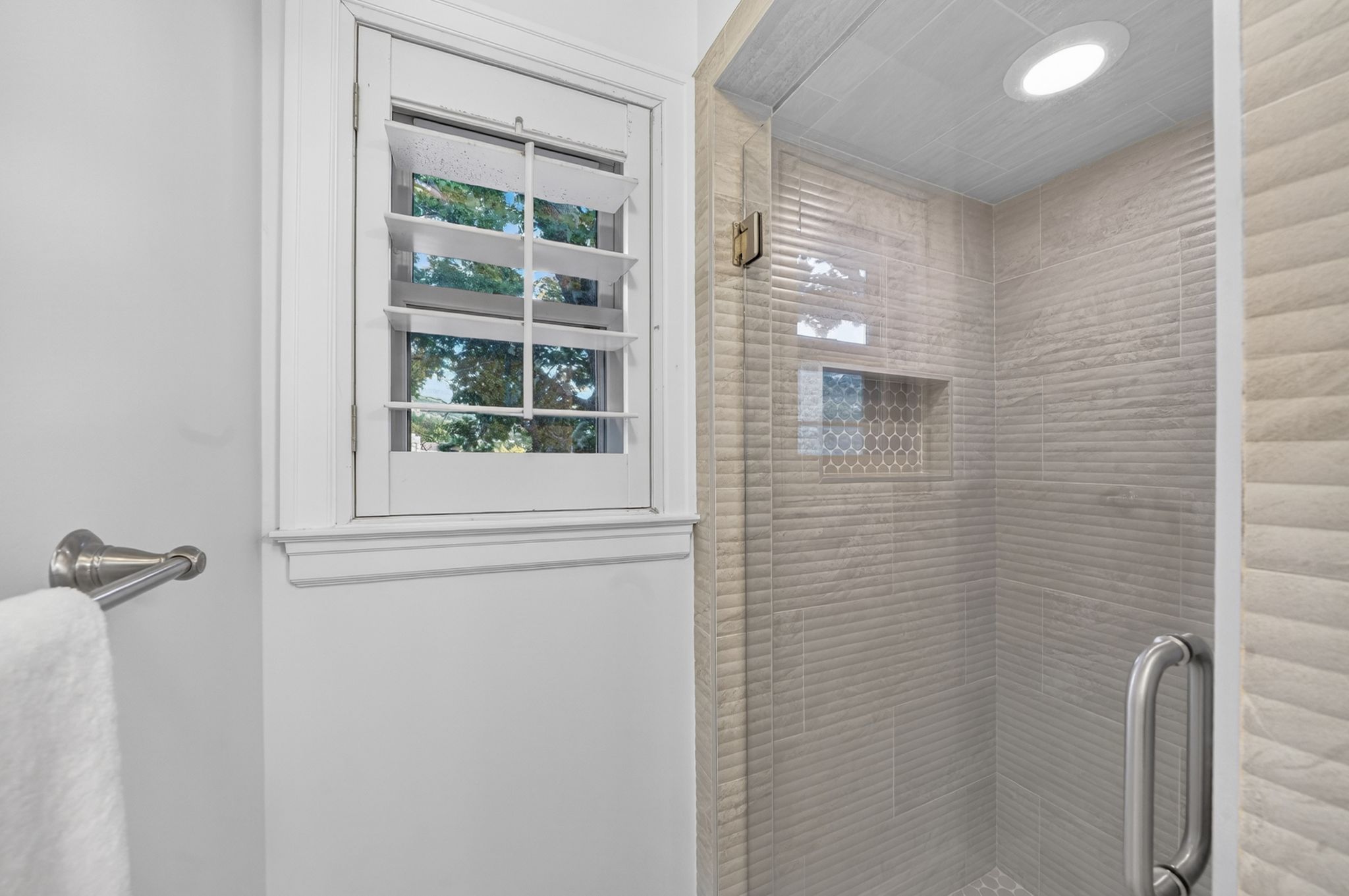 Glass-enclosed shower featuring textured wall tiles, a mosaic-tiled niche, and a recessed ceiling light