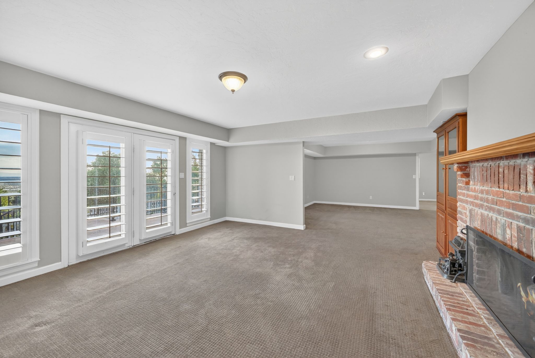 Spacious interior room featuring a brick fireplace, built-in wooden cabinetry, recessed lighting, and multiple windows with plantation shutters
