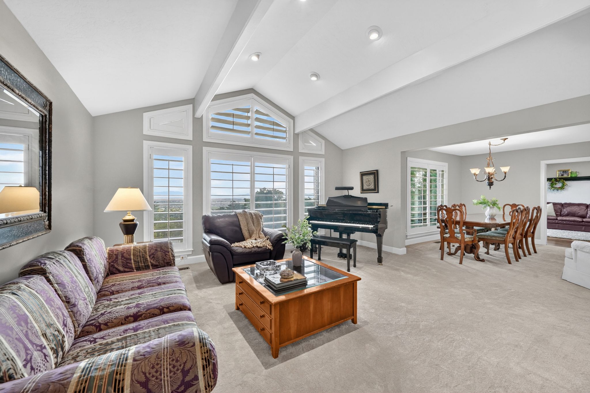 Vaulted ceilings with exposed beams complement the expansive window wall featuring plantation shutters