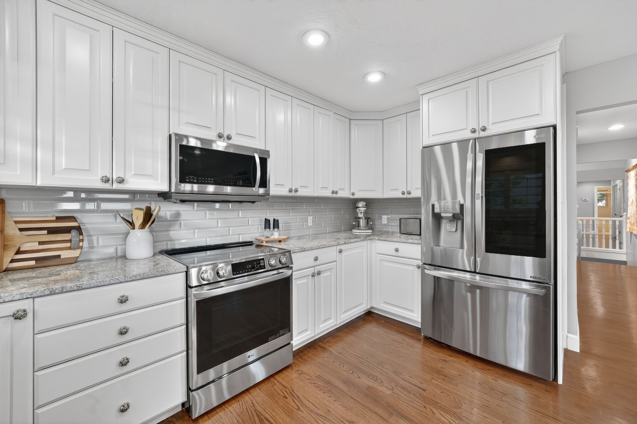 Kitchen featuring white shaker-style cabinetry, stainless steel appliances, light-colored countertops, a tile backsplash, and wood-finish flooring