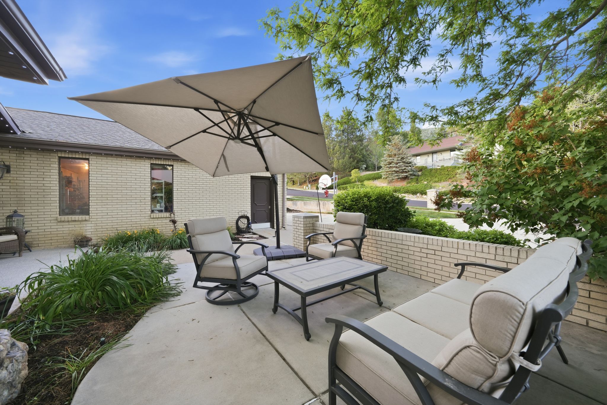 Concrete patio featuring a brick retaining wall and mature landscaping