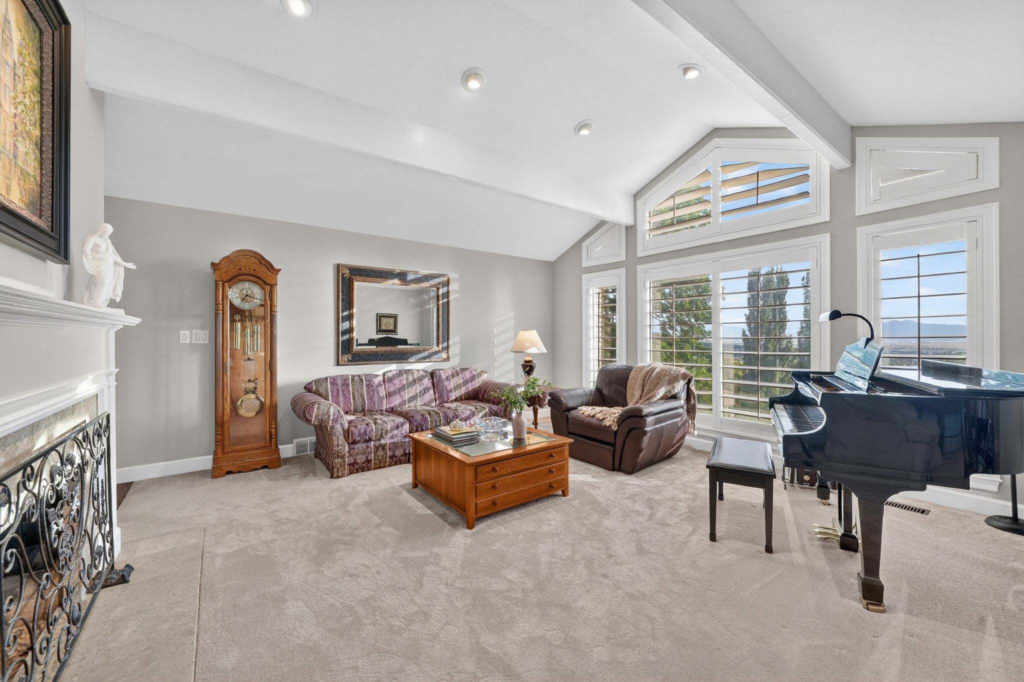 Spacious living area featuring vaulted ceilings with exposed beams, recessed lighting, and large windows with plantation shutters