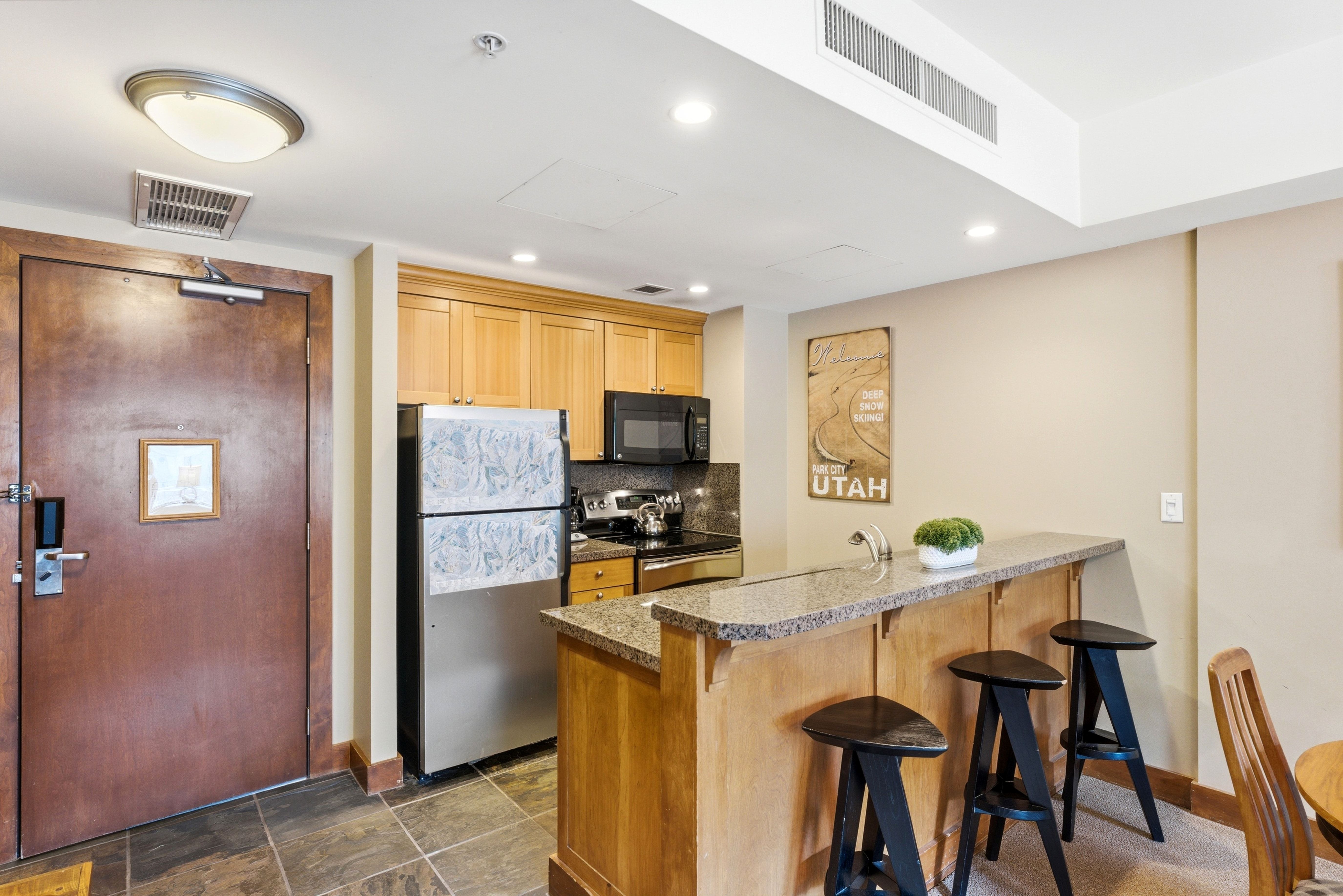 Kitchenette featuring stone-look flooring, light wood cabinetry, stainless steel appliances, a breakfast bar with stone-look countertop, and recessed lighting