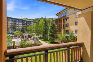 Balcony overlooking a community pool area with multiple lounge chairs, surrounded by mature evergreen trees and a paved walkway
