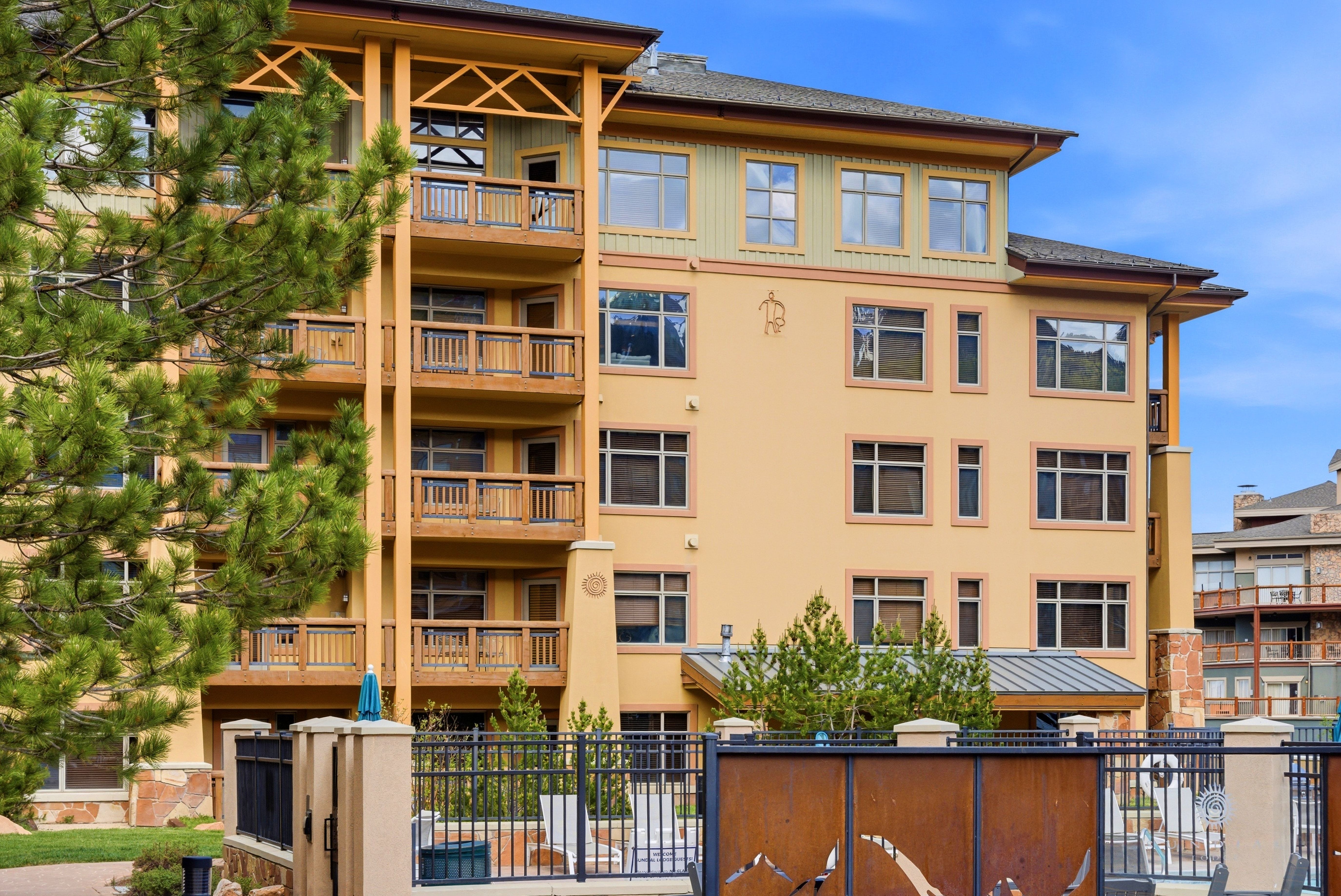 Multi-story building featuring stucco and siding exterior finishes, multiple private balconies with wood railings, a pitched roofline, and a decorative metal gate