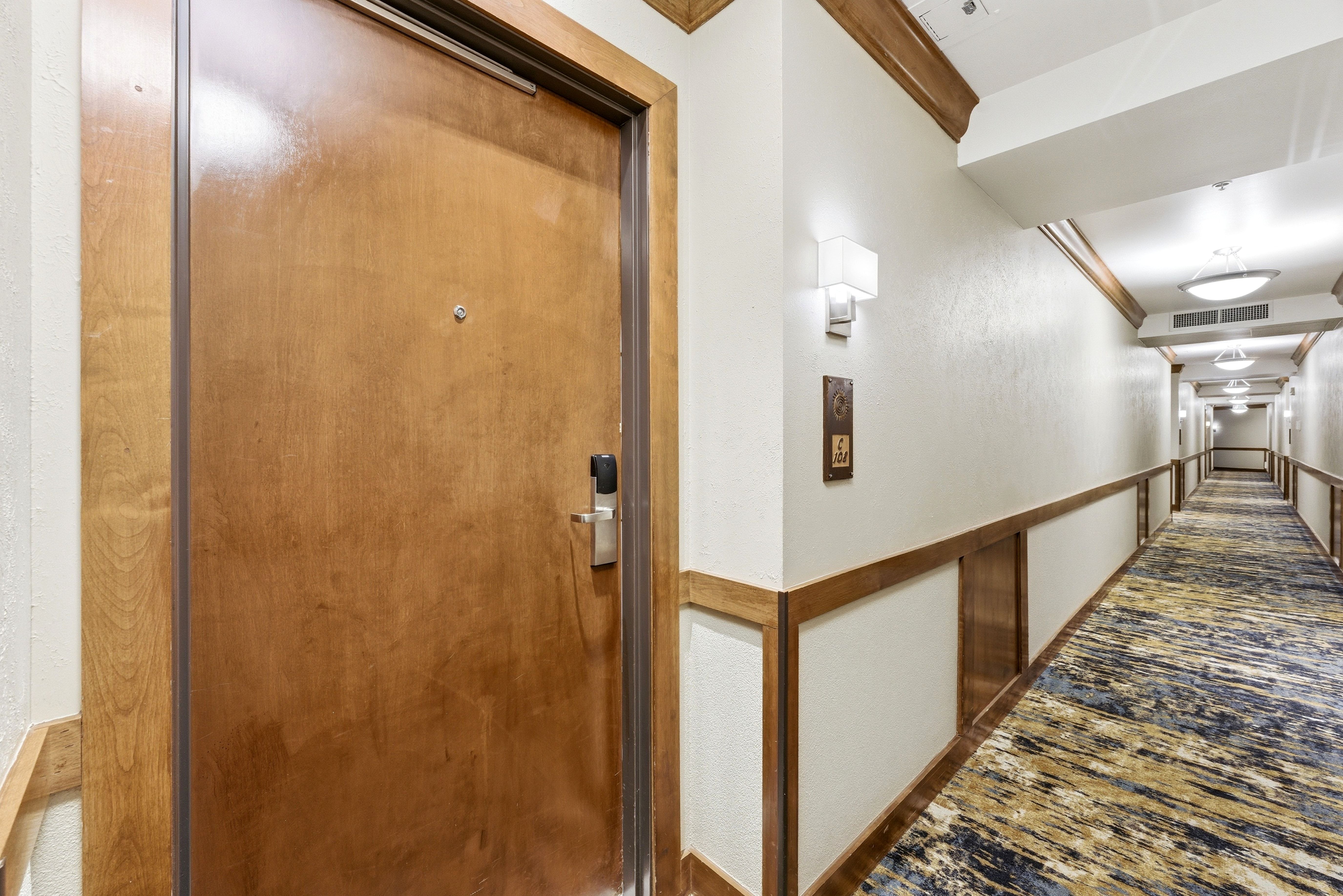 Entry door with modern key card access, wood-finish paneling, and contemporary wall sconces