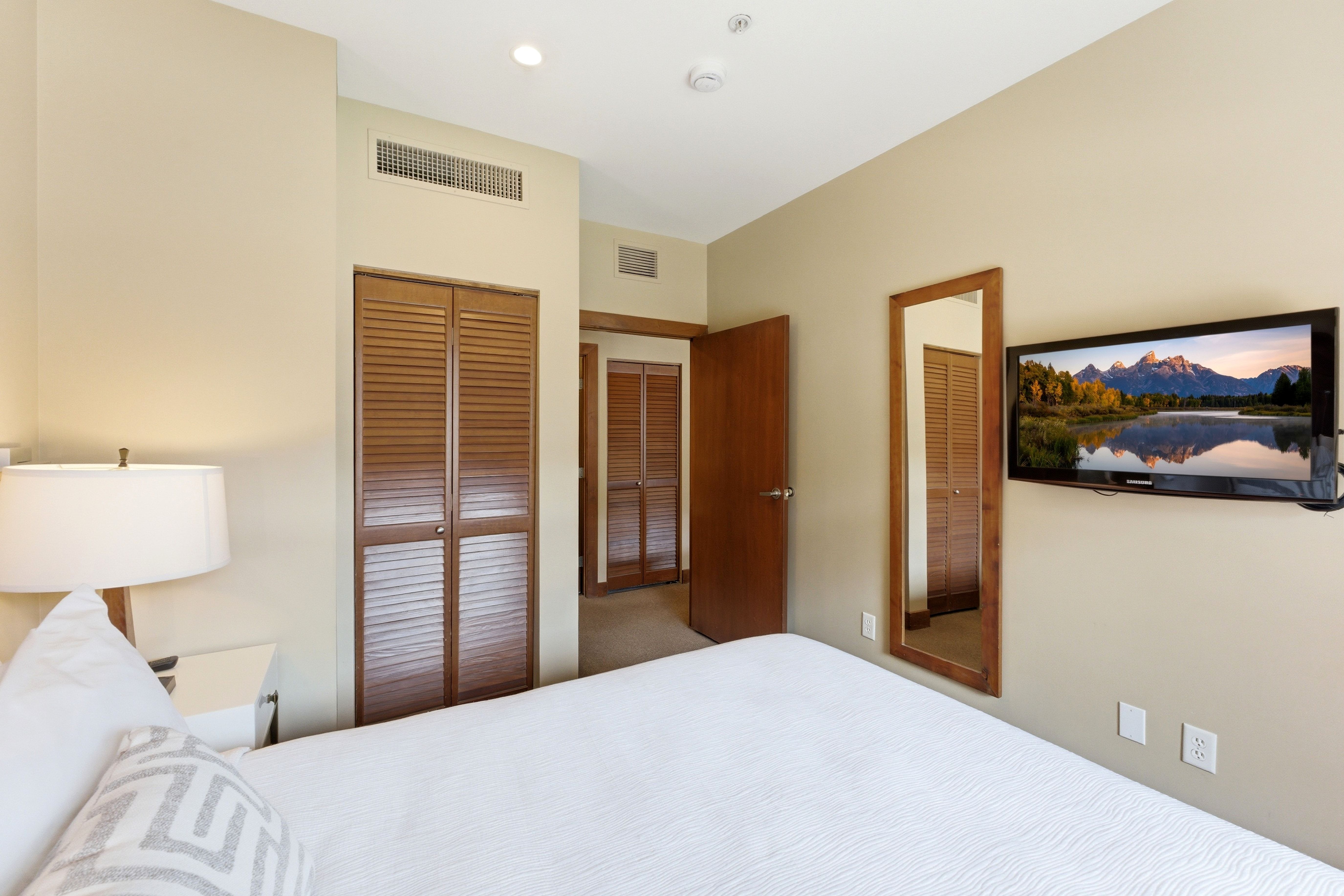 Bedroom featuring neutral wall paint, recessed ceiling lighting, a wall-mounted flat-screen television, and a full-length framed mirror