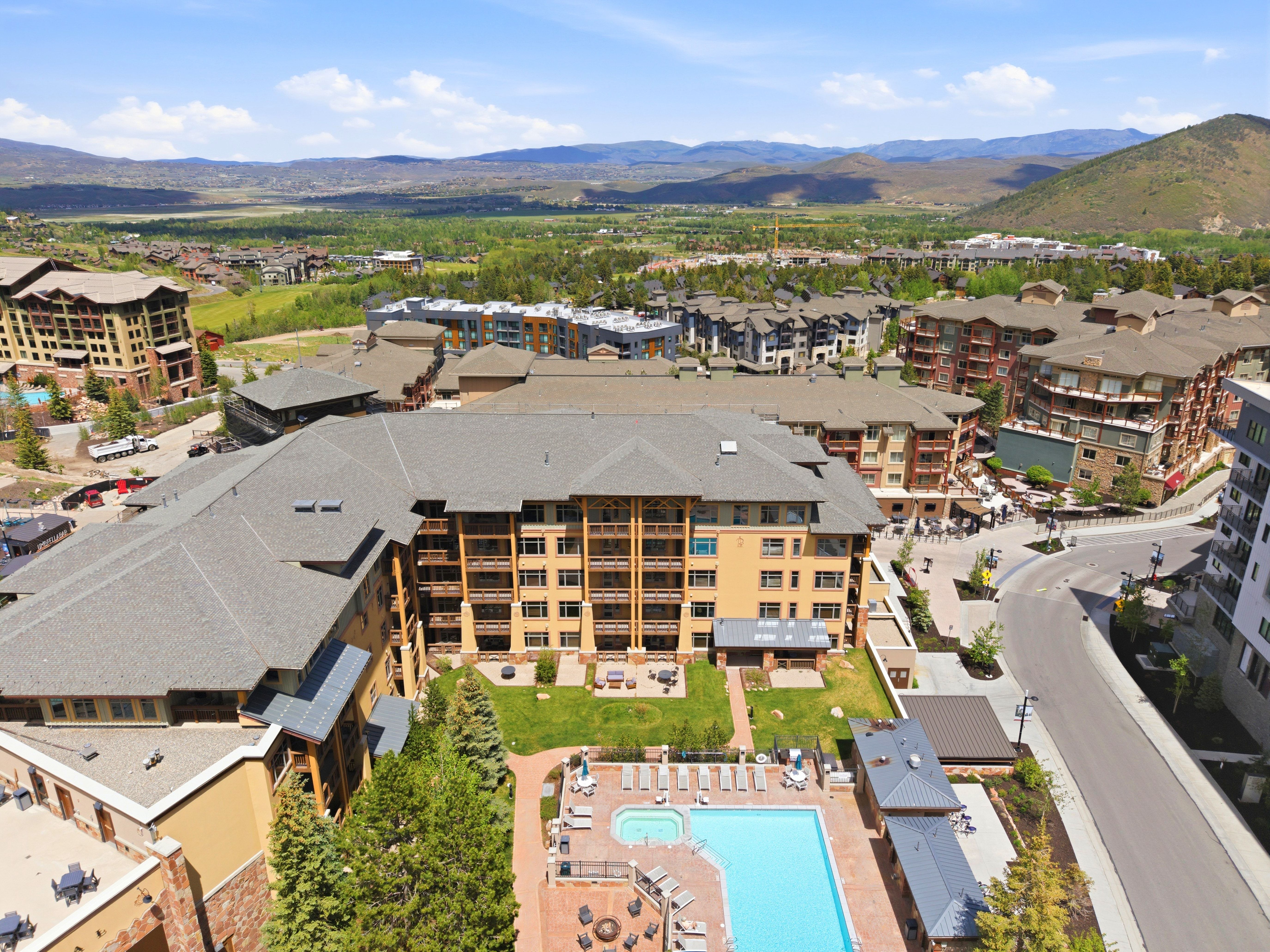 Multi-story building featuring multiple private balconies, a central courtyard with a manicured lawn, and an outdoor pool with a hot tub