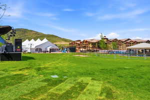 Expansive green lawn surrounded by a white picket fence, with a large event tent and multi-story buildings in the background