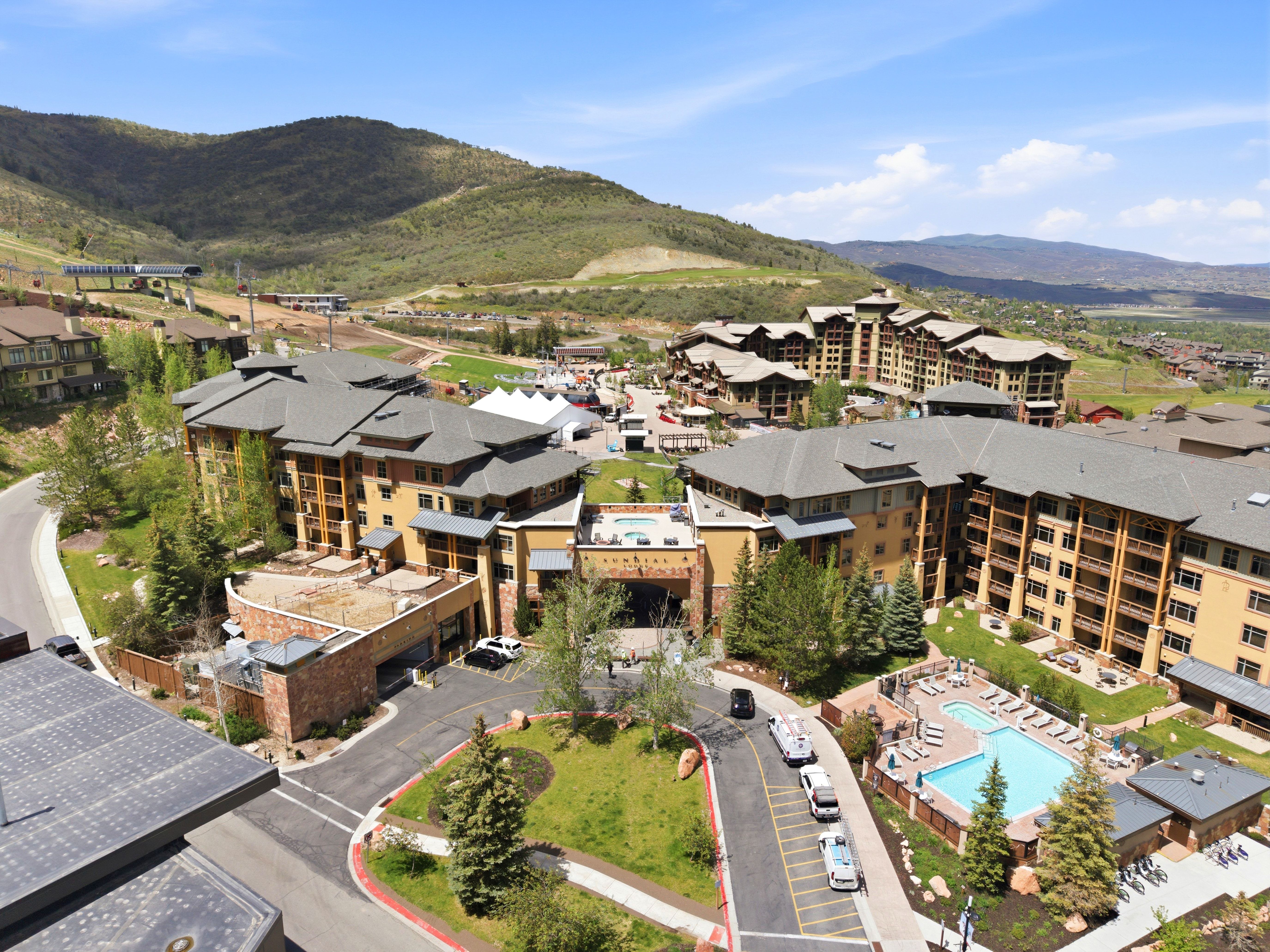 Mountain-backed residential complex featuring multiple buildings with balconies, a central resort-style swimming pool, and surrounding green spaces