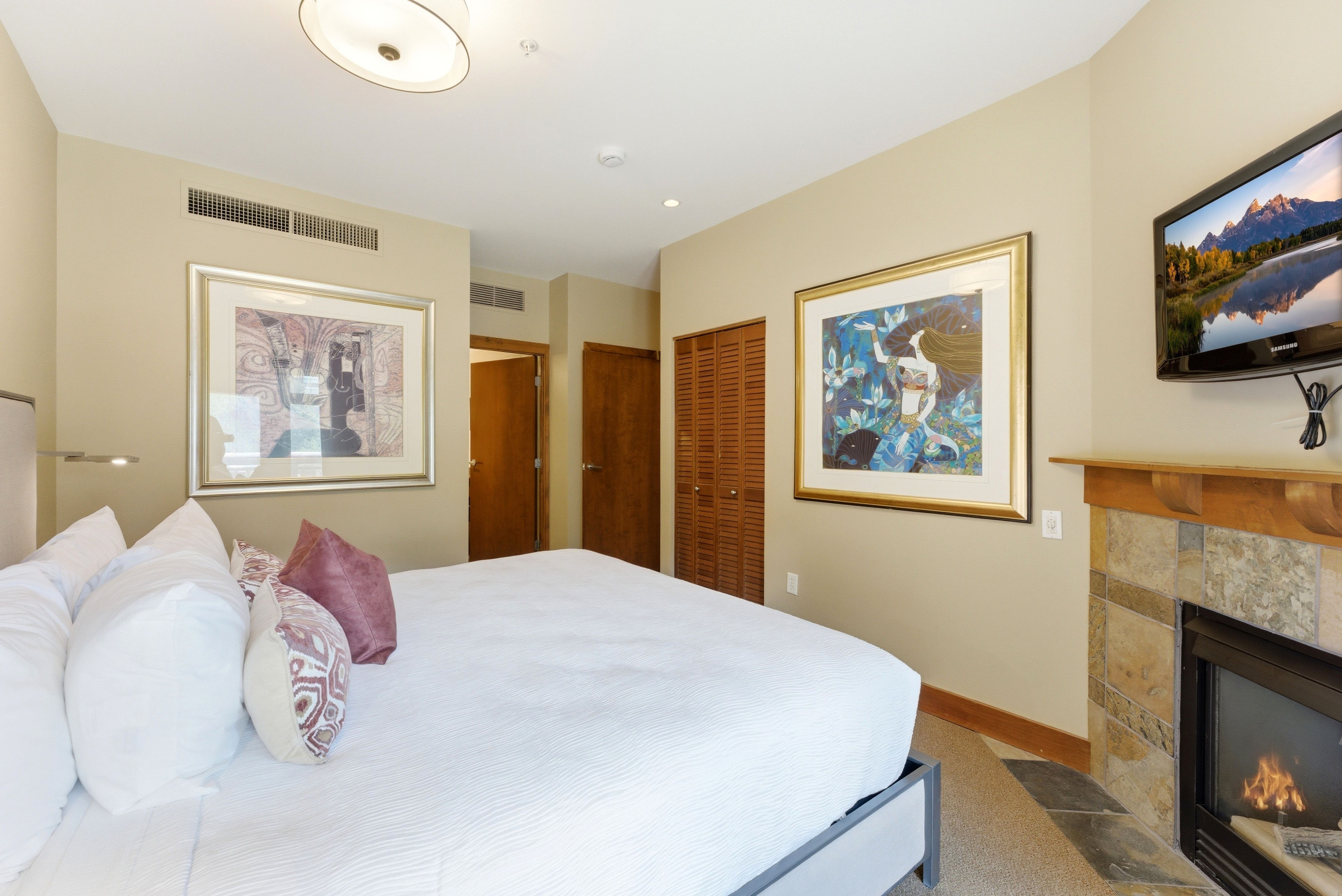Bedroom featuring a built-in fireplace with a stone surround and wood mantel, wall-mounted television, and a ceiling-mounted light fixture