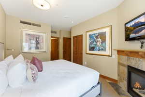 Bedroom featuring a built-in fireplace with a stone surround and wood mantel, wall-mounted television, and a ceiling-mounted light fixture