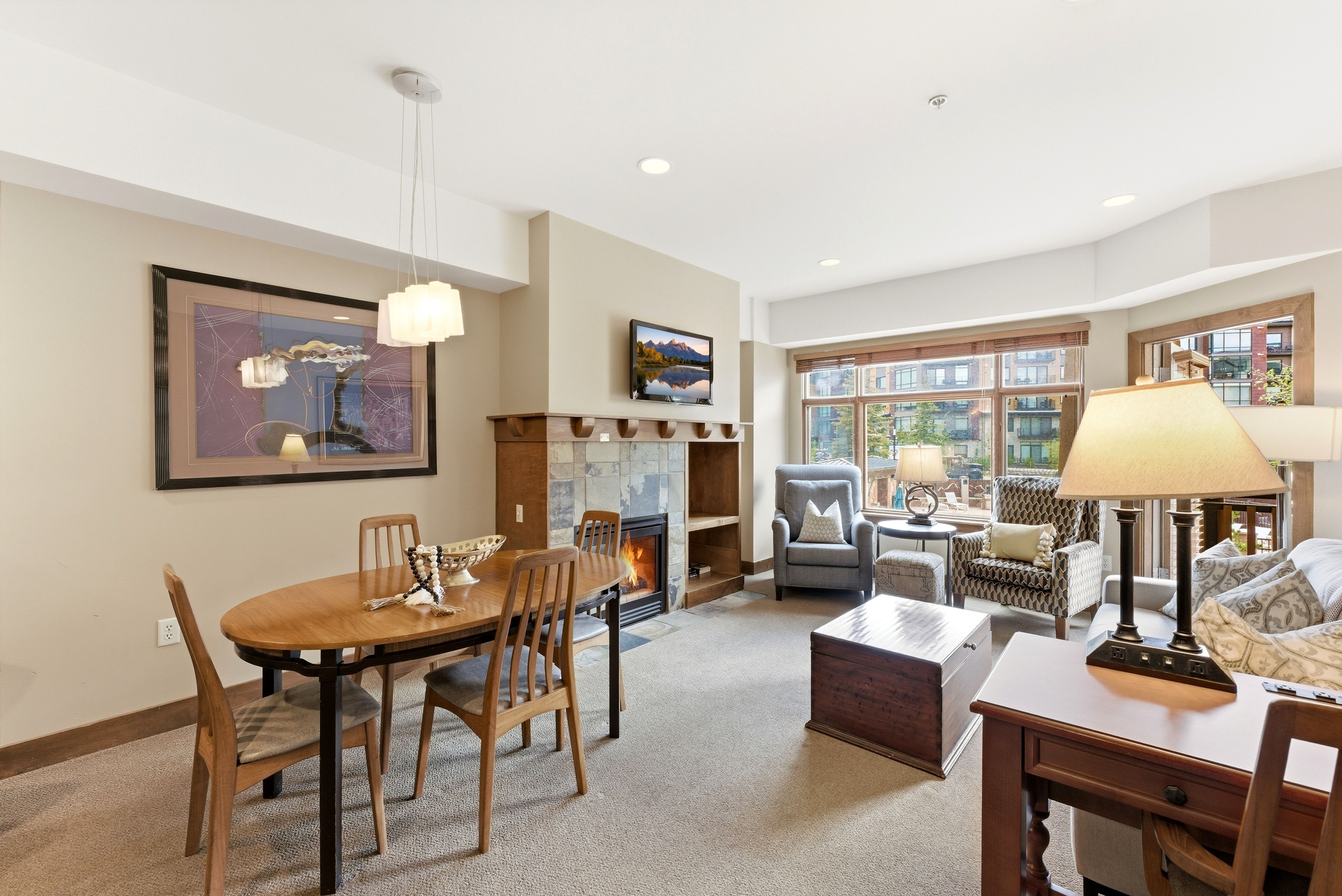 Open-concept living area featuring a stone-faced fireplace with wood mantel, large window array, recessed lighting, and a modern dining pendant light fixture