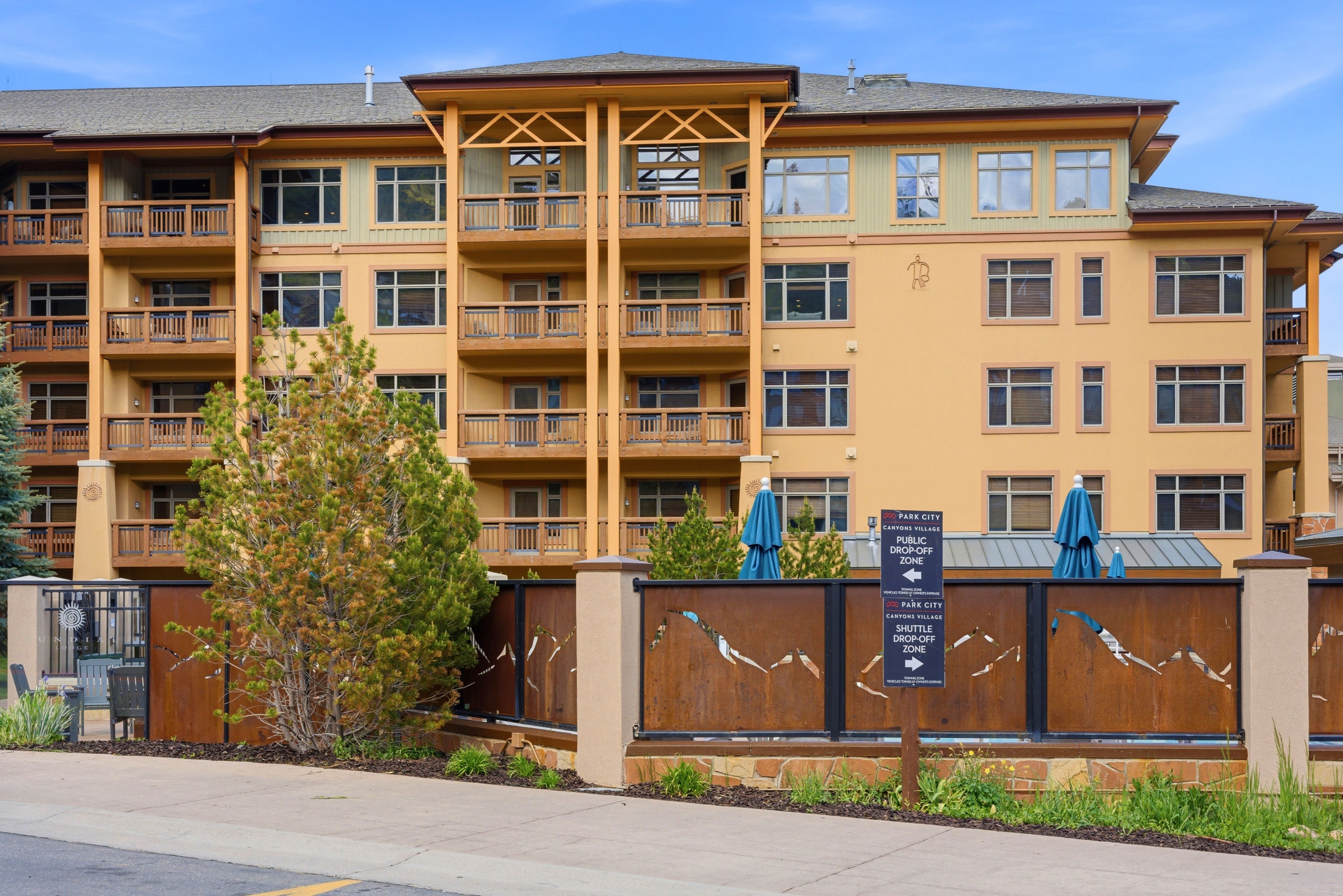 Multi-story property featuring numerous private balconies with wood railings, a neutral-toned stucco exterior, and a contemporary metal fence with artistic cutouts