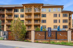 Multi-story property featuring numerous private balconies with wood railings, a neutral-toned stucco exterior, and a contemporary metal fence with artistic cutouts