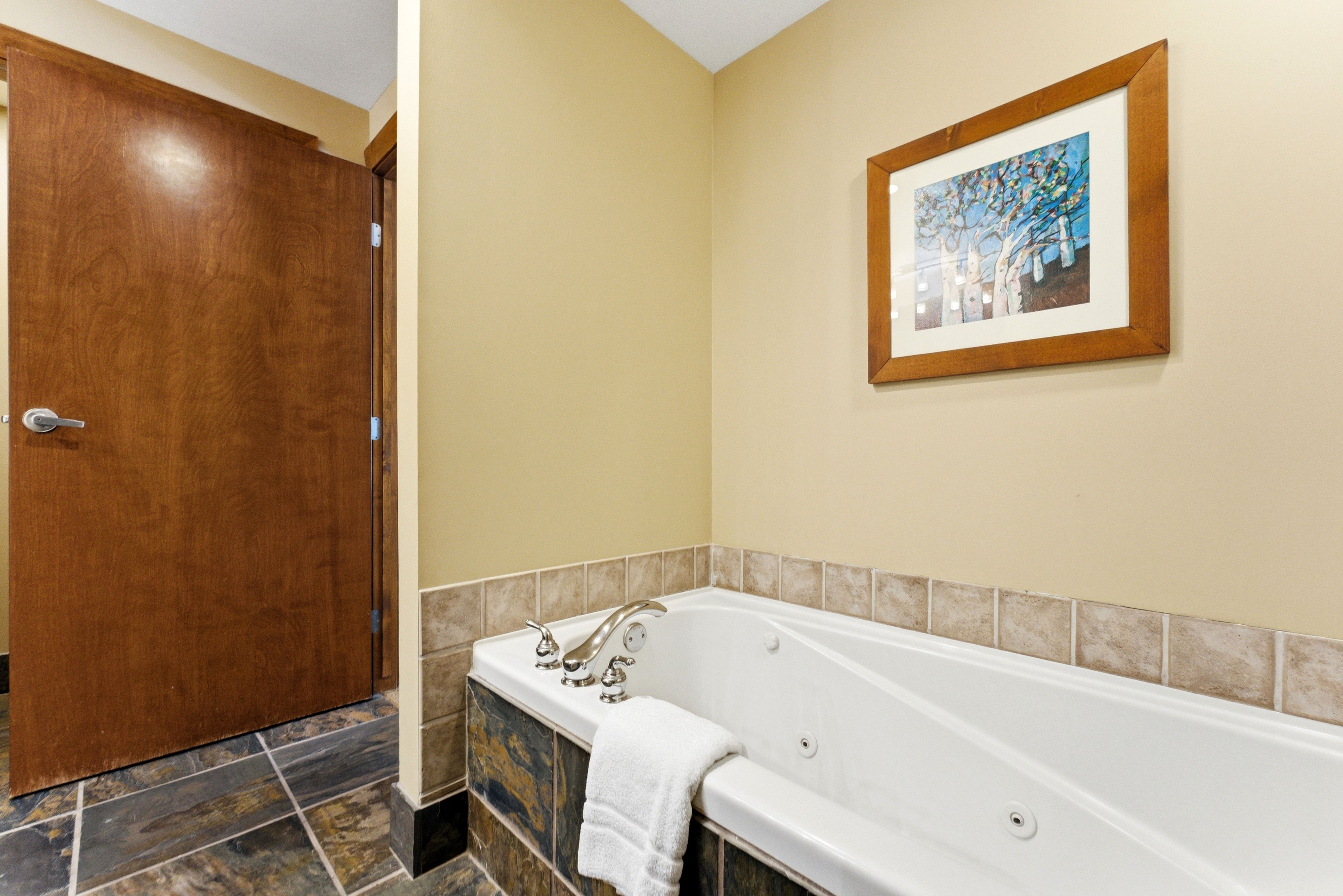 Jetted soaking tub with chrome fixtures, surrounded by stone-look tile