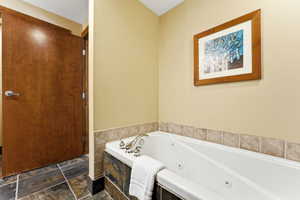 Jetted soaking tub with chrome fixtures, surrounded by stone-look tile