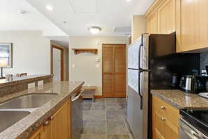 Kitchen featuring granite countertops, wood cabinetry, stainless steel appliances, and slate-finish floor tiling