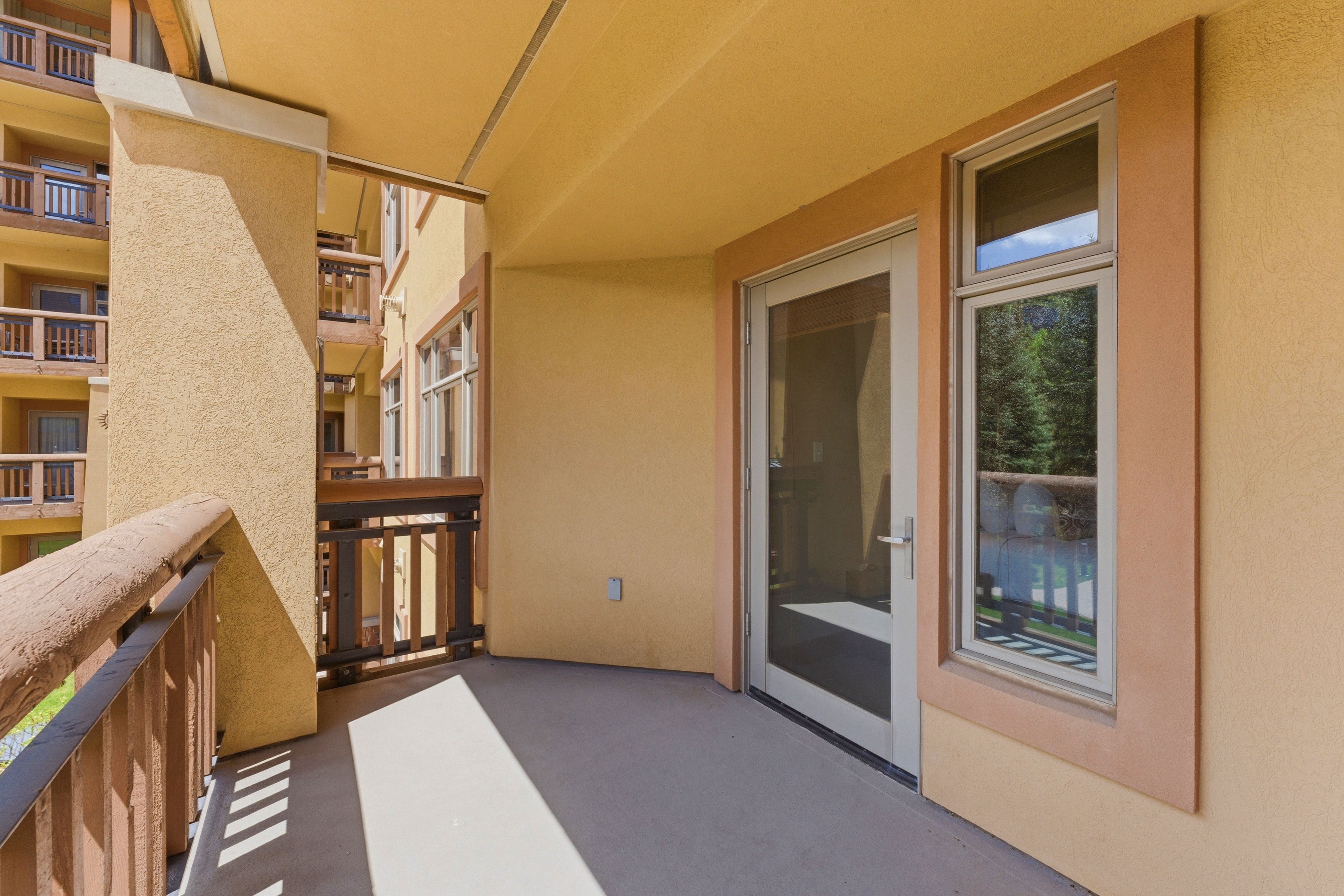 Private balcony with textured stucco exterior, concrete flooring, glass-paneled door, and adjacent vertical window