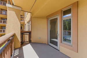 Private balcony with textured stucco exterior, concrete flooring, glass-paneled door, and adjacent vertical window