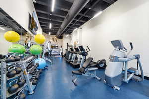 Fitness center featuring blue rubberized flooring, exposed ductwork, modern track lighting, and a mirrored wall