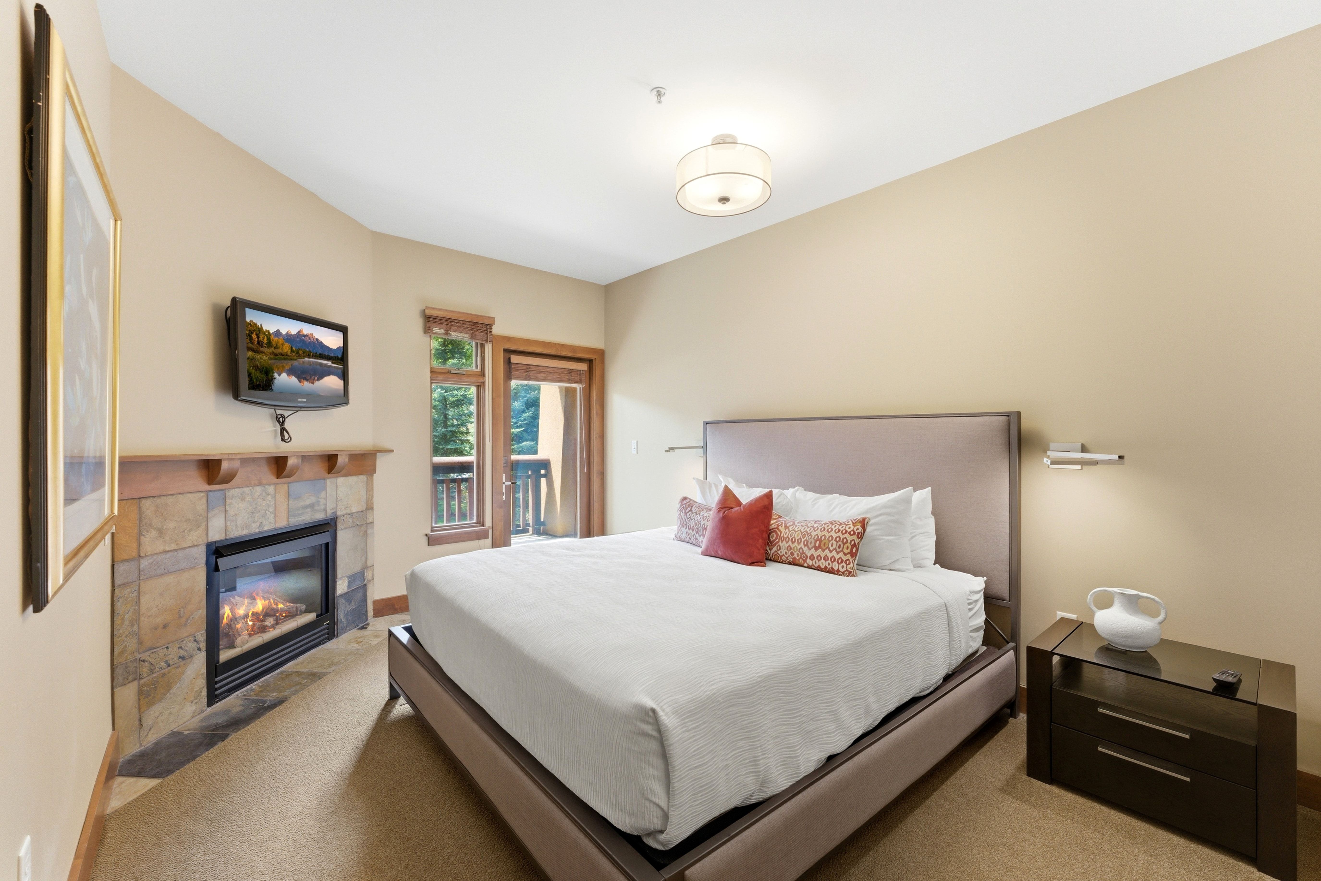 Bedroom featuring a gas fireplace with stone surround and wood mantel, mounted television, and outdoor access