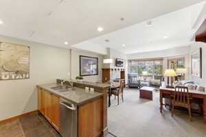 Open-concept living area featuring a kitchen island with dual sinks and stainless steel appliances, a dining space, and a living room with an integrated television