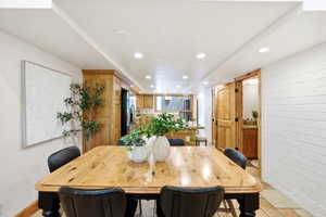 Hardwood dining table with custom turned legs, recessed lighting, white brick accent wall, wood-finish flooring, and natural wood doors