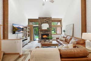 Spacious living area featuring a stone fireplace, vaulted ceiling with a ceiling fan, and large windows