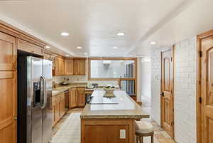 Kitchen featuring wood cabinetry, stainless steel appliances, a center island with a cooktop, stone countertops, and recessed lighting