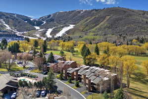 Aerial perspective showcasing a community of multi-level properties with dark roofs, surrounded by mature trees and manicured green spaces