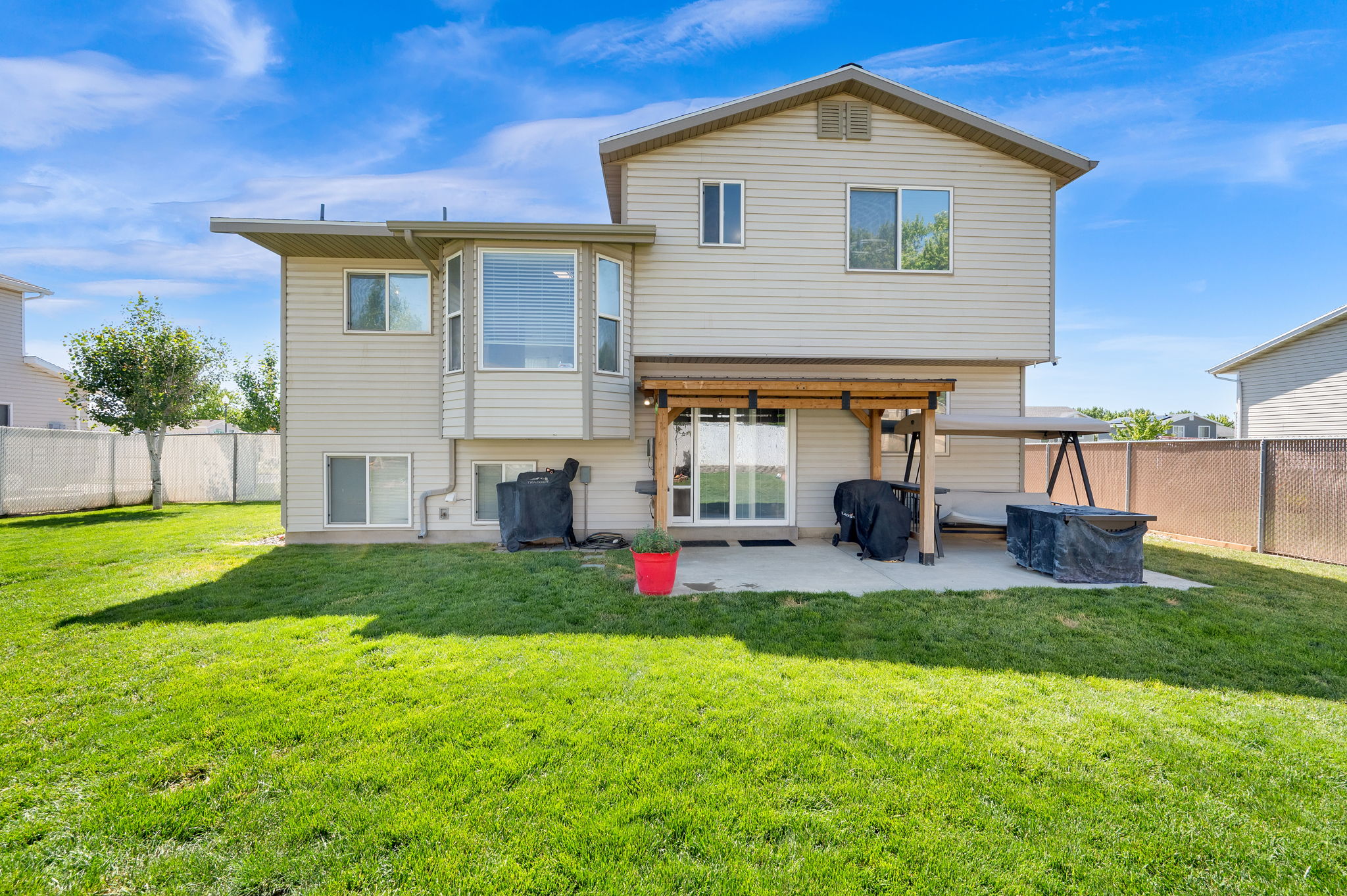 Expansive green lawn with a concrete patio, sliding glass door access, and an overhead wood pergola