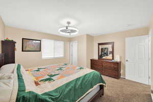 Spacious bedroom featuring neutral wall tones, carpet flooring, a window with blinds, and a ceiling fan with integrated lighting