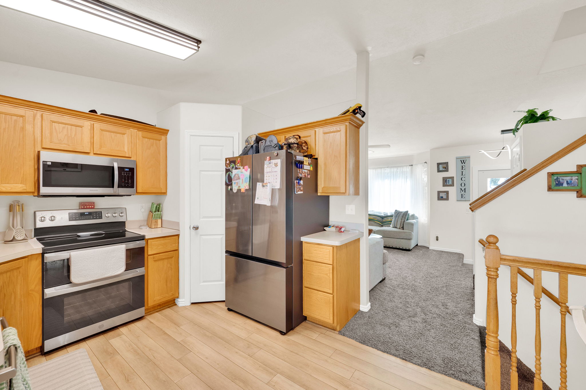Kitchen featuring wood-finish flooring, stainless steel appliances, light wood cabinetry, and a light-toned countertop