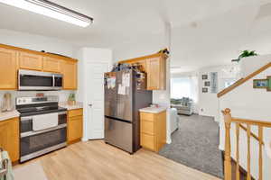 Kitchen featuring wood-finish flooring, stainless steel appliances, light wood cabinetry, and a light-toned countertop