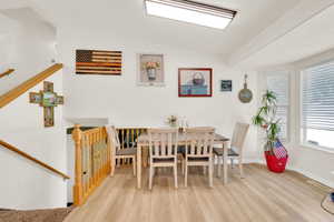 Dining area featuring light wood-finish flooring, white walls, and a large window with blinds