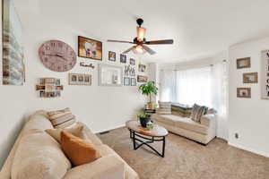 Carpeted living space featuring a bay window, ceiling fan with integrated lighting, and a neutral color palette