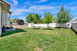 Expansive green lawn with a privacy fence, mature trees, a concrete patio, and a storage shed
