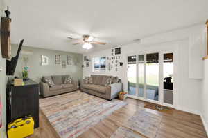 Spacious living area featuring wood-finish flooring, a ceiling fan, and light green wall accents