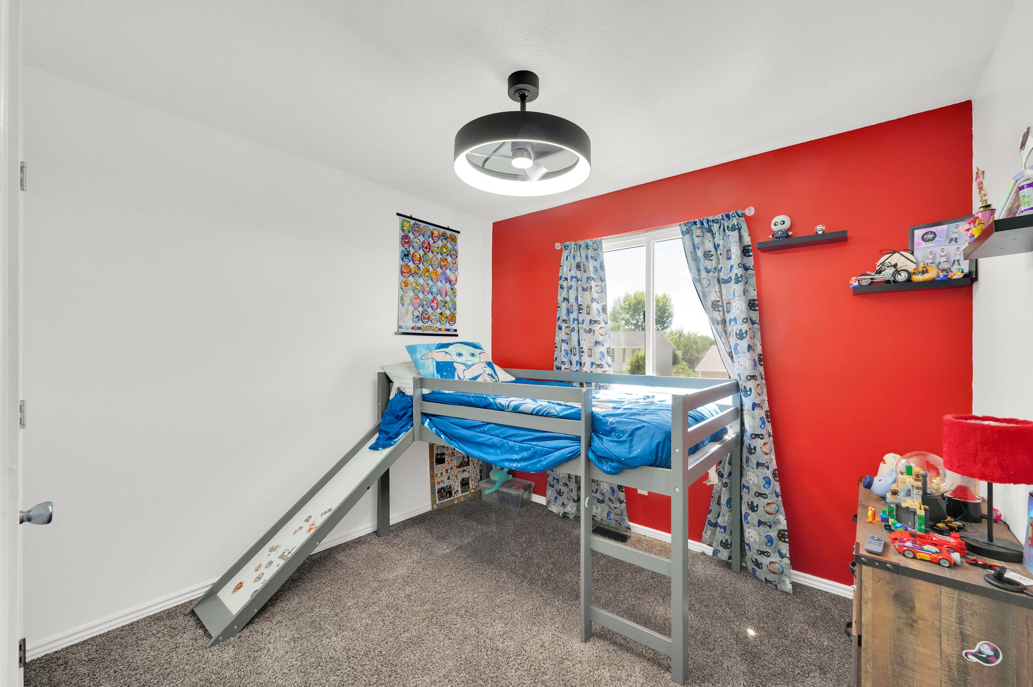 Spacious room featuring a window with natural light, a ceiling fan with integrated lighting, a red accent wall, and neutral carpet flooring