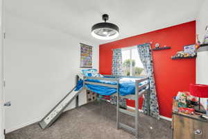 Spacious room featuring a window with natural light, a ceiling fan with integrated lighting, a red accent wall, and neutral carpet flooring