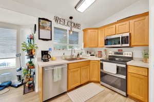 Kitchen featuring wood-finish cabinetry, stainless steel appliances, light countertops, and wood-finish flooring