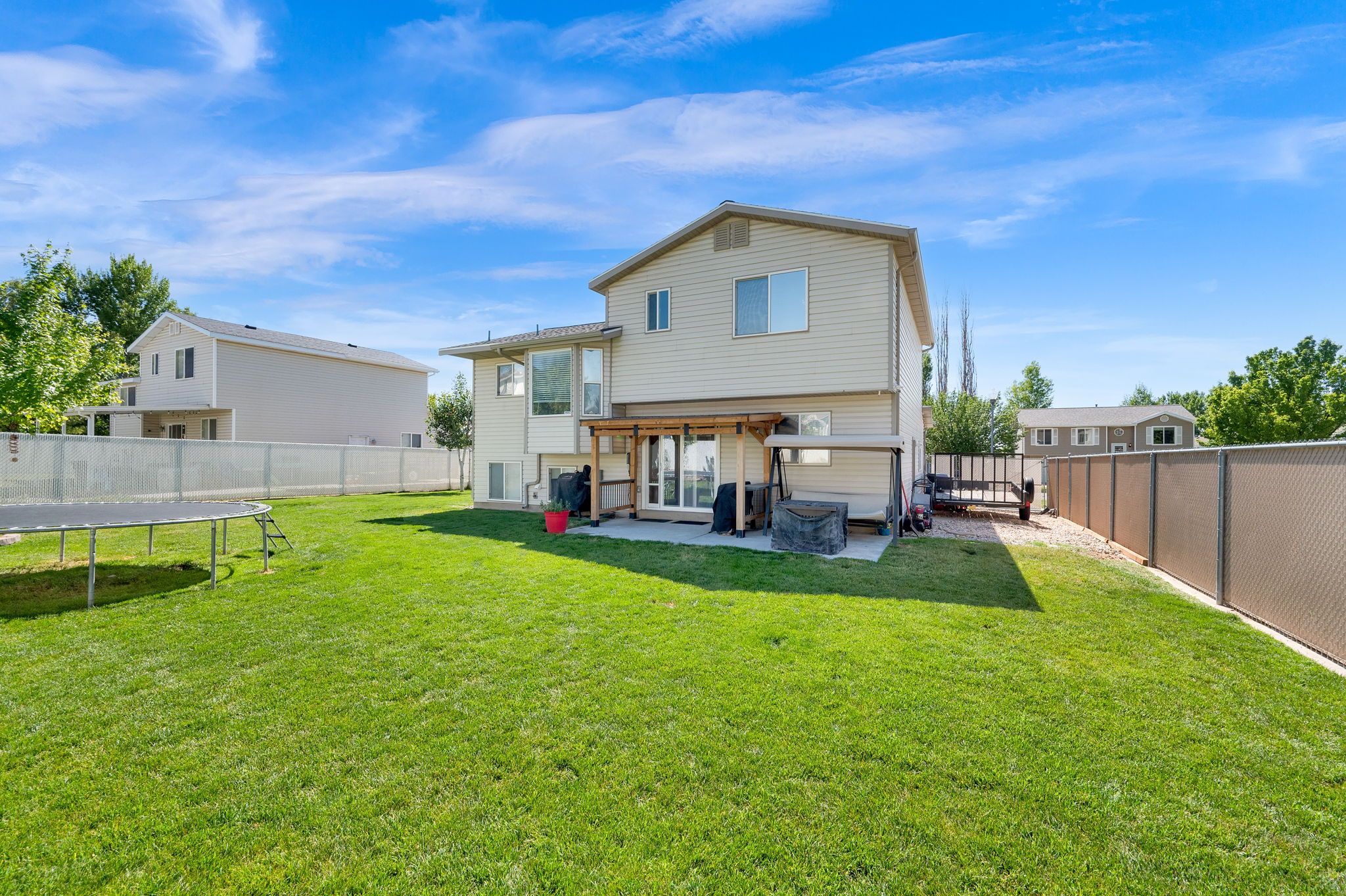 Expansive rear yard featuring a verdant lawn, a concrete patio, and a wood pergola