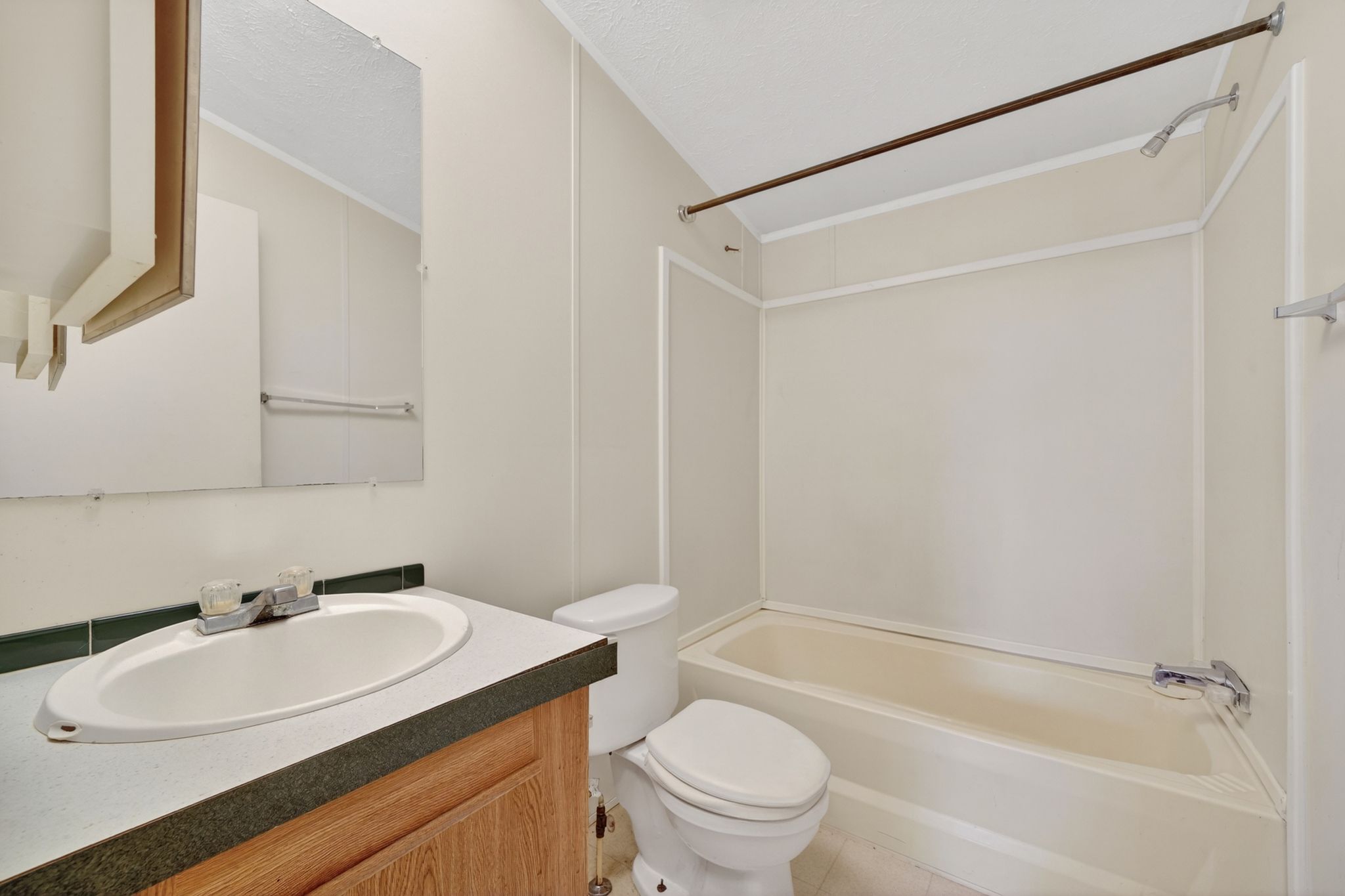 Full bathroom featuring a single vanity with wood-finish cabinetry, a white oval sink, and a built-in bathtub with shower