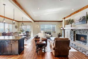 Open-concept living area featuring wood-finish flooring, exposed ceiling beams, recessed lighting, and a stone fireplace