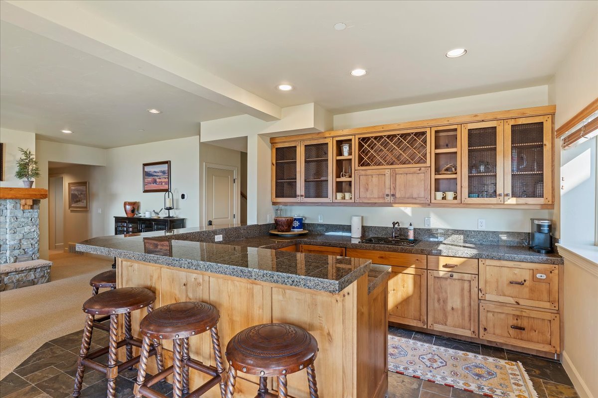 Wet bar with a granite countertop, undermount sink, and wood-finish cabinetry featuring glass-paneled doors and a wine rack