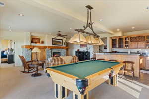 Recreational space featuring a built-in wet bar with wood cabinetry and a stone countertop, a stone fireplace with a substantial wood mantel, recessed lighting, and a ceiling fan