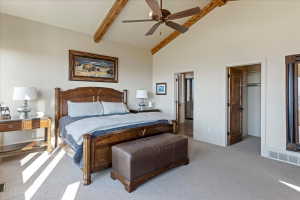 Vaulted ceiling with exposed wood beams, ceiling fan, and light-toned carpeting