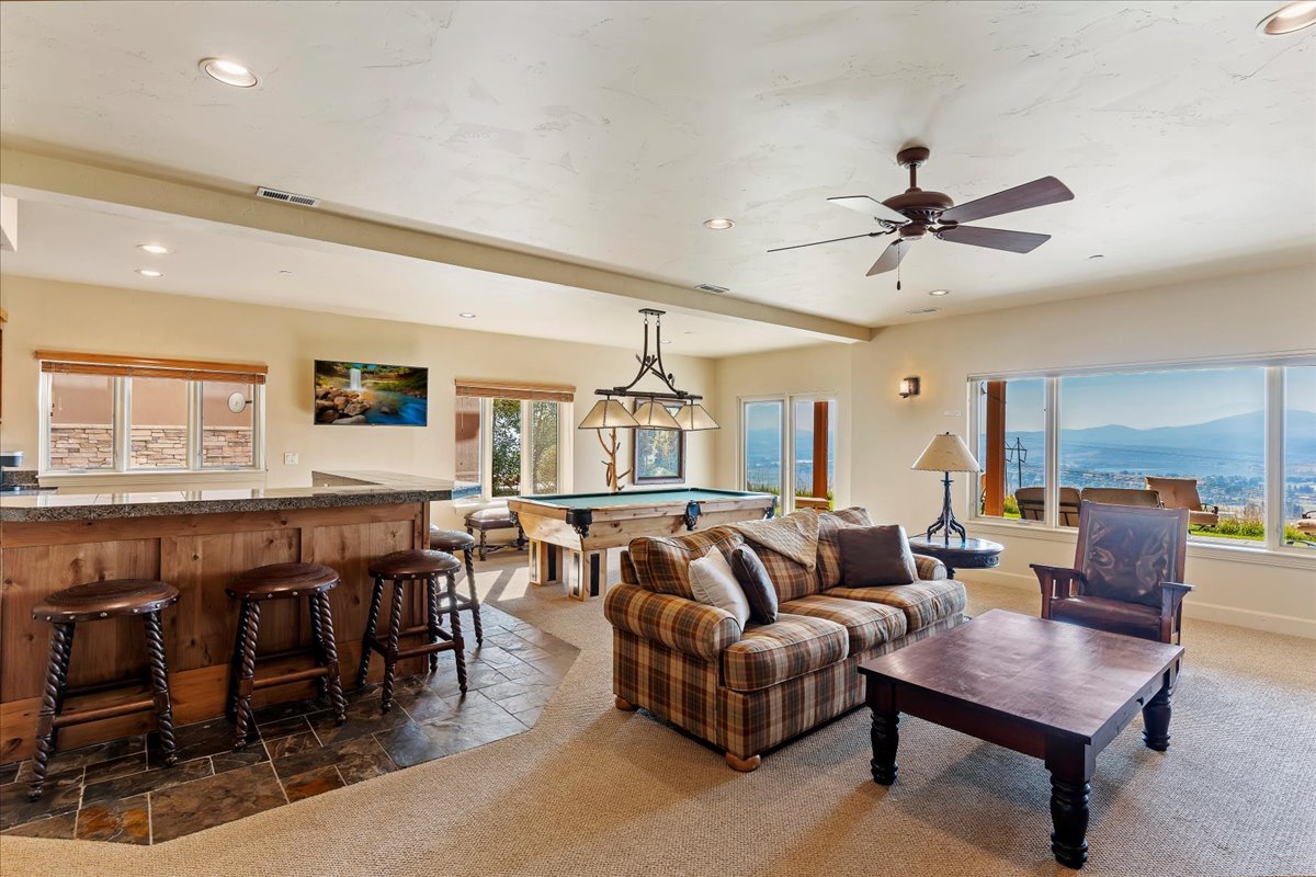 Entertainment space featuring a wood-panel wet bar with stone-finish countertop, recessed lighting, and a ceiling fan