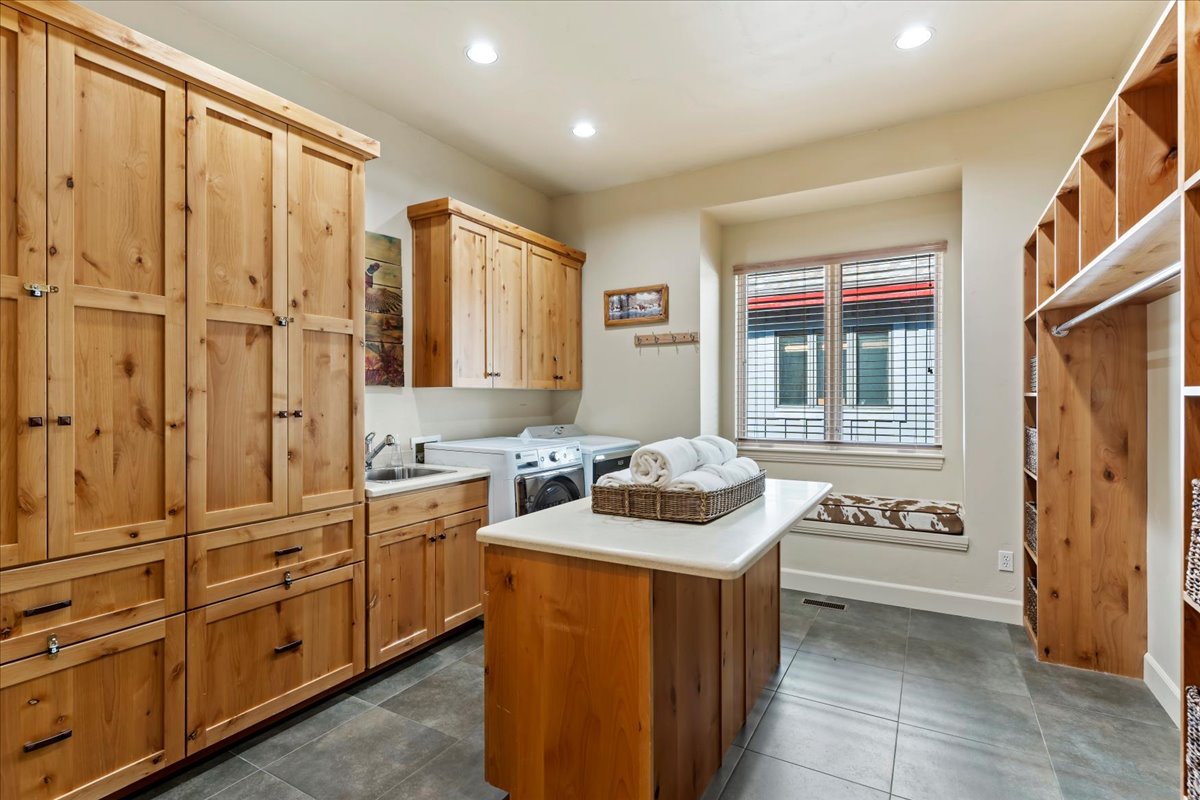 Spacious utility room featuring extensive natural wood cabinetry, a built-in sink, durable tile flooring, a functional center island with a light-colored countertop, and a window with a built-in bench